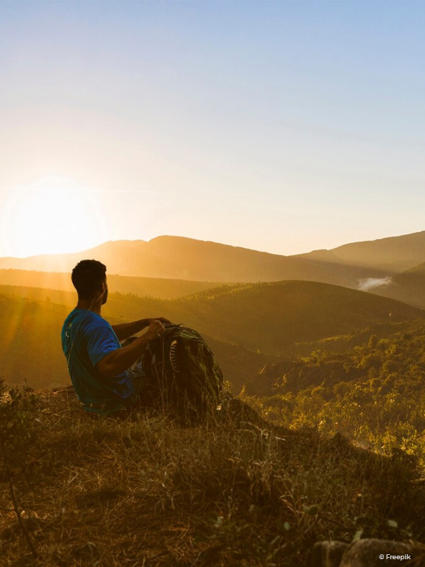 Man sitting in nature watching the hills at sunset.