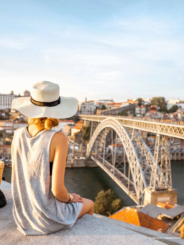 Tourist woman with sunny hat overlooking the city of Porto, the Dom Luis bridge and the Douro river.