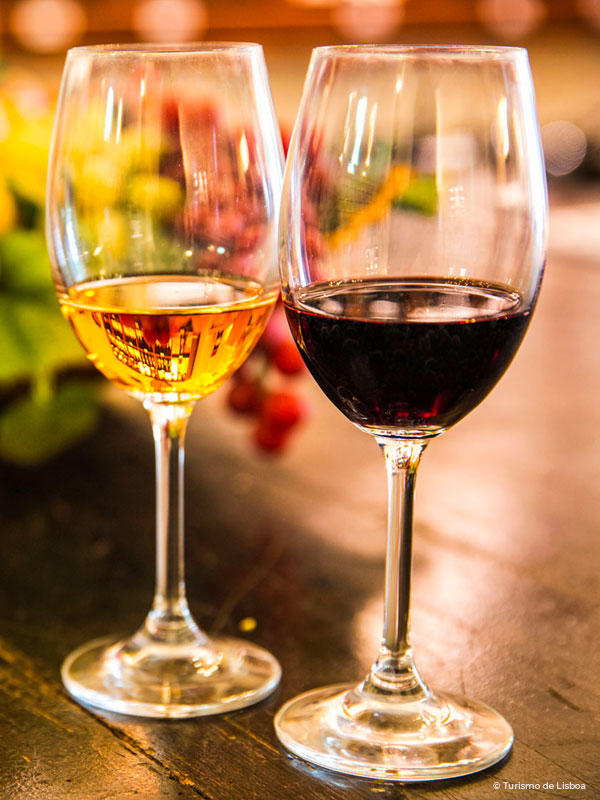 Two wine glasses on top a table. One glass filled with wite wine and another glass filled with red wine.